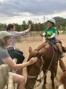A wrangler high-fives a small child on a horse