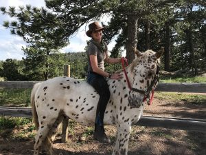 A girl smiles while riding a spotted horse bareback.