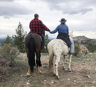 Two guests hold hands while on horseback.