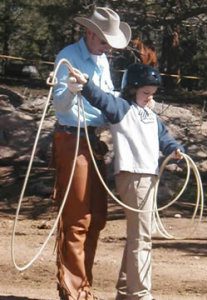 A wrangler teaches a boy how to swing a rope.