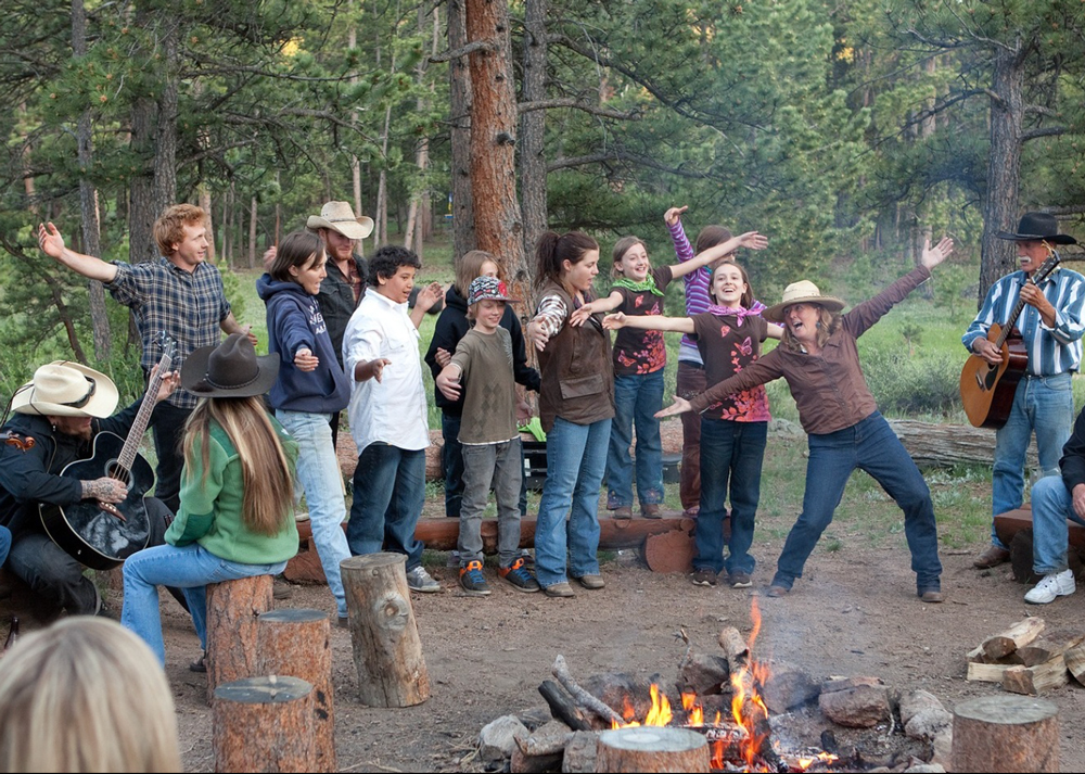 Guests gather around the campfire at Sundance Trail Guest Ranch, enjoying cowboy singing and a fun, rustic evening.