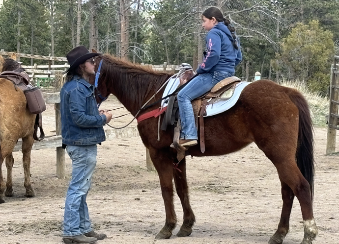 A wrangler guides a 9-year-old girl on horseback in the arena, teaching her safe riding techniques at Sundance Trail Guest Ranch.